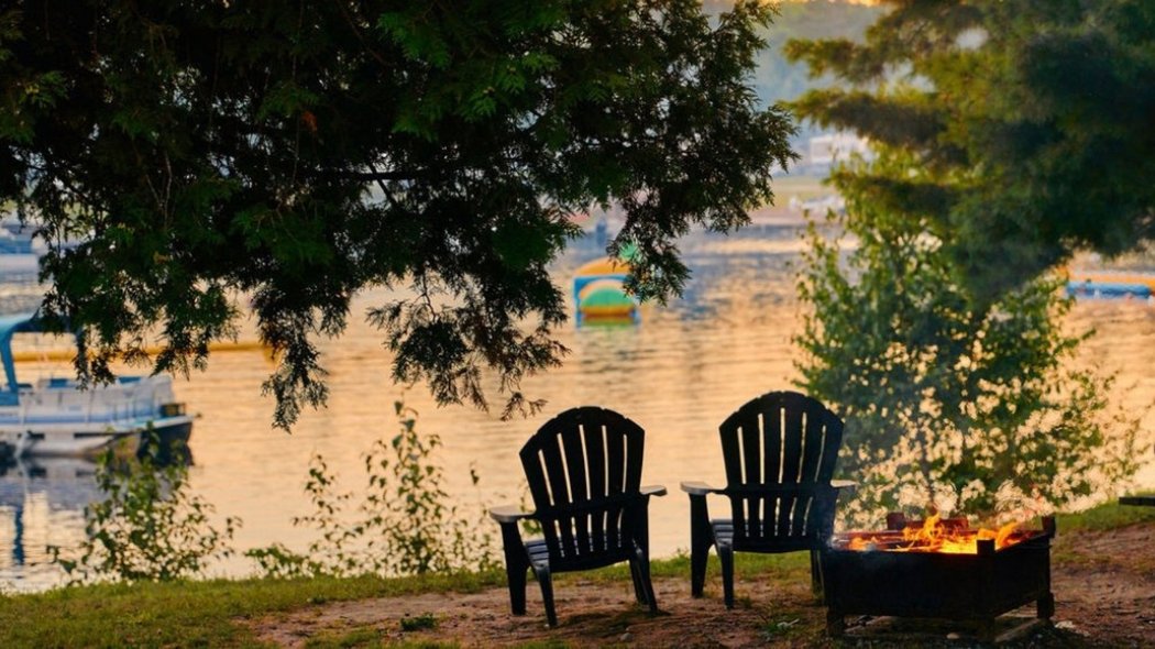 Deux chaises de camping devant un feu et un lac