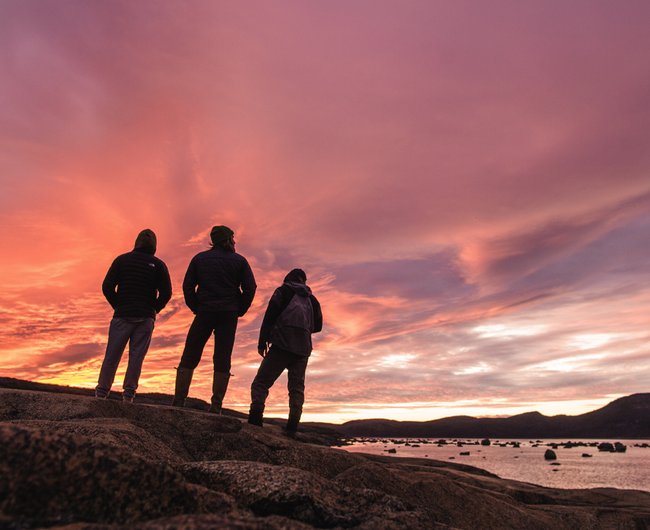 Trois personnes debout sous un couché de soleil rose