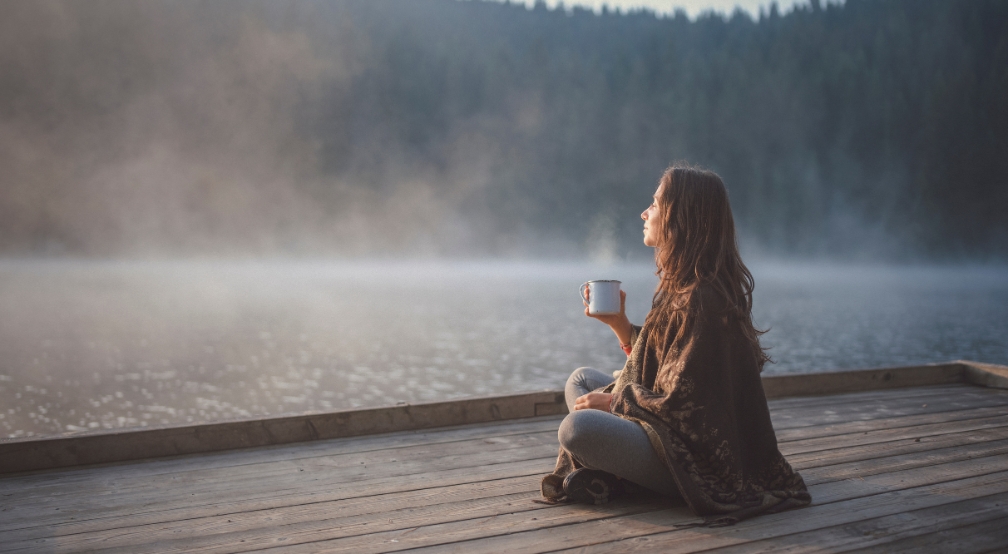 Femme assise sur un quai avec une tasse de café, ambiance brumeuse